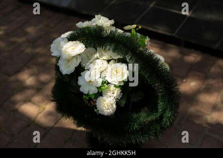 Gedenkkranz aus weißen Blumen. Korb mit Blumen. Künstliche Pflanzen im Sonnenlicht. Stockfoto