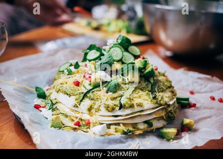 Chaotisch Esstisch mit weichem Fokus bunt vegetarisch gesundes Gericht - Tortilla Pie mit Granatapfel und Avocado, Gurke und Käse Stockfoto