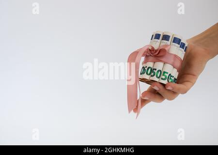 Weibliche Hand hält Banknoten von 50 Euro in Rollen, gebunden mit rosa Geschenkband. Stockfoto