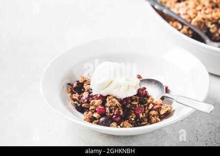 Beerenkrümelkuchen mit einer Kugel Eis auf weißem Teller, grauer Hintergrund. Stockfoto