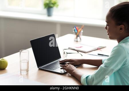 Teenager afroamerikanische Mädchen Schüler tippen auf Laptop mit Mockup leeren Bildschirm und studieren Stockfoto