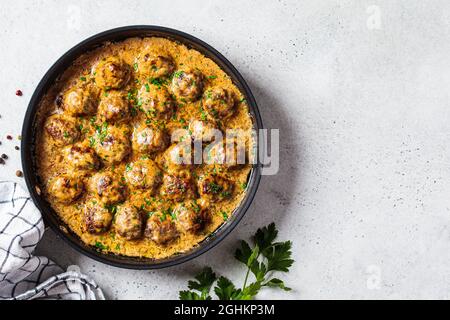 Schwedische Fleischbällchen in cremiger Sauce in schwarzer Bratpfanne, grauer Hintergrund, Draufsicht. Skandinavisches Lebensmittelkonzept. Stockfoto