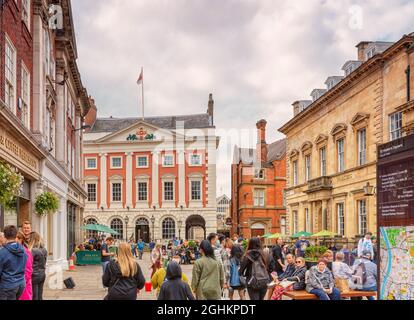 Öffentlicher Platz mit historischen Gebäuden und Menschen saßen auf Bänken. Im Hintergrund befindet sich ein Haus aus dem 18. Jahrhundert und ein wolkiger Himmel ist darüber. Stockfoto