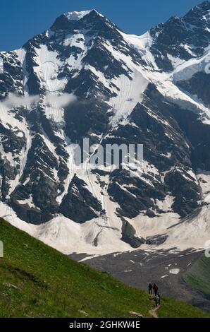 Eine Gruppe von Wanderern mit Rucksäcken wandern entlang einer Bergkette vor dem Hintergrund verschneiter Berge. Das Konzept der Reise zum Berg Stockfoto