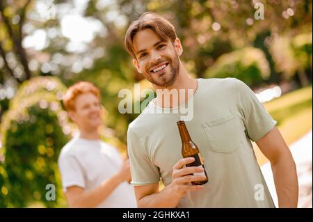 Lächelnder bärtiger Typ mit Flasche und Freund dahinter Stockfoto