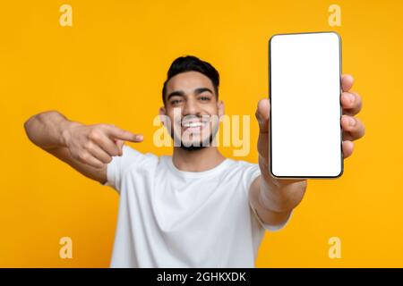 Glücklicher arabischer Kerl, der auf das Handy mit leerem Bildschirm zeigt Stockfoto