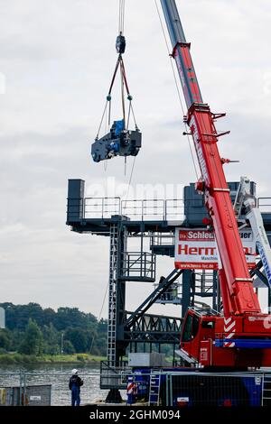 07. September 2021, Schleswig-Holstein, Osterrönfeld: Ein Kran trägt einen Balancer auf ein Gerüst unter der Rendsburg-Eisenbahnbrücke. Fünfeinhalb Jahre nach ihrer Beschädigung haben die Arbeiten an der Installation einer neuen schwimmenden Fähre begonnen. Sie war am 8. Januar 2016 mit einem Schiff in schlechter Sicht kollidiert. Die historische schwimmende Fähre wurde so stark beschädigt, dass sie abgebaut werden musste. Foto: Frank Molter/dpa Stockfoto