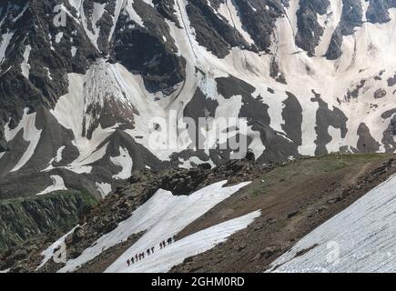 Eine Gruppe von Wanderern mit Rucksäcken wandern entlang einer Bergkette vor dem Hintergrund verschneiter Berge. Das Konzept der Reise zum Berg Stockfoto