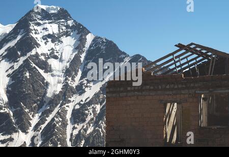 Altes verlassenes Haus in den Bergen. Ruinen einer Hütte ohne Dach auf dem Hintergrund der schneebedeckten Gipfel der Berge. Nahaufnahme Stockfoto