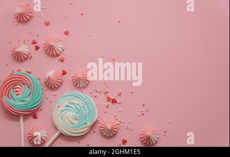 Pastellfarbene Merengues in Mintblau und Pink sowie süße Bonbons auf rosa Pastelltönen. Süßigkeitenkonzept. Copyspace. Glückwunschkarte zum Geburtstag. Stockfoto