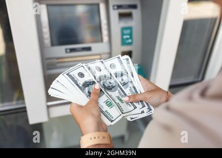 Junge arabische Frau in Hijab zieht Geld ab, zählt Dollar in der Nähe von geldautomaten mit leerem Bildschirm Stockfoto