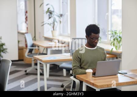 Ernster Softwareentwickler, der Kaffee trinkt und auf dem Laptop kodiert, im Freiraum-Büro die Stirn runzelte Stockfoto
