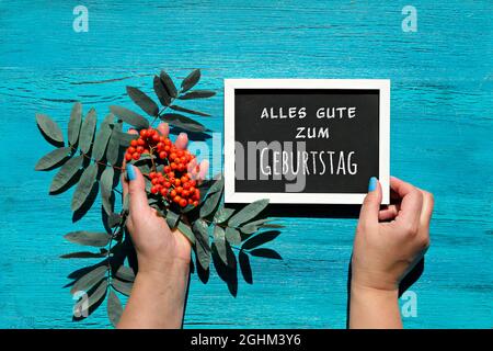 Deutscher Text alles gute zum Geburtstag bedeutet Alles Gute zum Geburtstag. Natürliche Herbstdekorationen. Orange Eberesche auf türkisfarbenem Holz. Flach liegend, Draufsicht. Fallen Stockfoto
