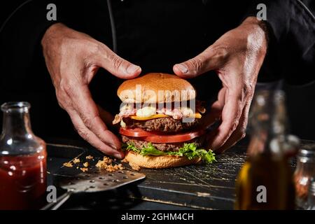 Gourmet-Burger mit Doppeldecker-Rindfleisch, Speck und Käse, über leckeren hausgemachten Hackfleischpasteten und frischen Salatzutaten auf einem gerösteten oder einem Grill Stockfoto