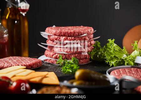 Stapel frisch zubereiteter, hausgemachter Hacksteaks für traditionelle Hamburger, umgeben von verschiedenen Salat- und Käsezutaten mit ausgewählten f Stockfoto