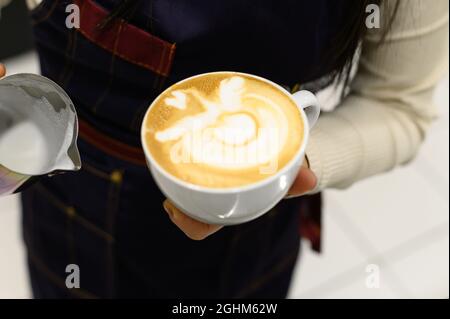 Hände eines jungen Barista, der Kaffee-Latte-Kunst zubereitet Stockfoto