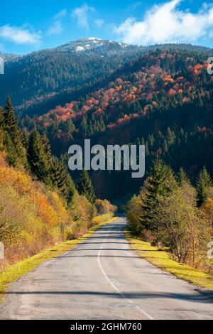 Landstraße in den Bergen. Schöne Herbstlandschaft an einem hellen sonnigen Morgen. Bäume in bunten Laub auf dem Weg. Flauschige Wolken am Himmel Stockfoto