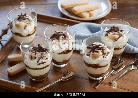 Hoher Winkel von appetitlichen Tiramisu Dessert in Gläsern auf Holztablett mit Löffeln auf dem Tisch platziert Stockfoto