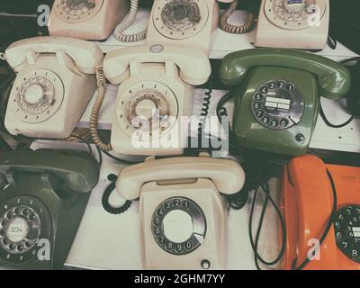 Viele alte Telefone mit Drehzifferblättern, die in hellen Räumen auf Holzregalen angeordnet sind, sind hochwinklig Stockfoto