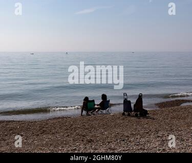 Zwei unverkennbare Damen, die am Meer sitzen und ihre Füße im Wasser kühlen, Worthing, West Sussex, Großbritannien, September 2021 Stockfoto