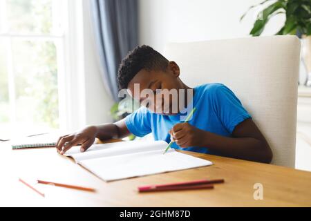 afroamerikanischer Junge, der im Wohnzimmer am Tisch sitzt und Hausaufgaben macht Stockfoto