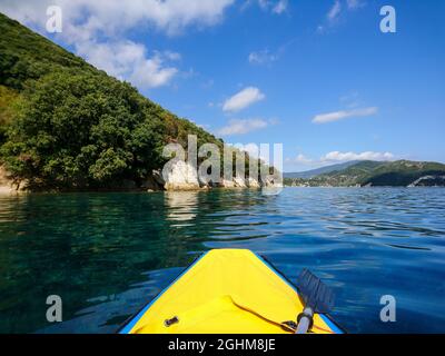 Gelbe Bootsnase und paddeln auf der blauen klaren ruhigen Bucht des Ionischen Meeres, Blick vom Boot aus. Schöne Wolken Reflexion und malerische grüne Hügel Küste. Lefkada Insel in Stockfoto