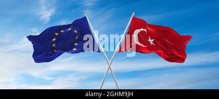 Flaggen der Europäischen Union und der Türkei winken im Wind auf Fahnenmasten gegen den Himmel mit Wolken am sonnigen Tag. Symbolisieren Beziehung, Dialog zwischen zwei Stockfoto