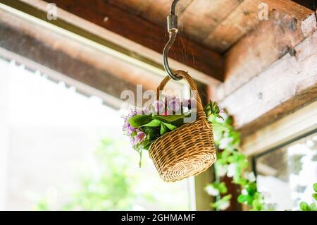 Gefälschte Blumen in einem Korb, der an einer staubigen Decke hängt Stockfoto