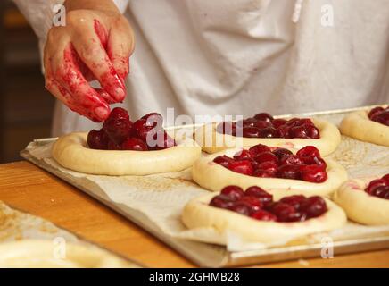 Die Frau auf dem Bild macht gefüllte Obstkuchen. Hände füllen Kuchen Hefeteig mit Erdbeeren. Arbeiten Sie in der Bäckerei. Stockfoto