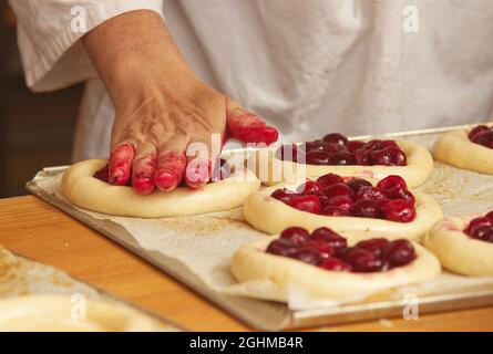 Die Frau auf dem Bild macht gefüllte Obstkuchen. Hände füllen Kuchen Hefeteig mit Erdbeeren. Arbeiten Sie in der Bäckerei. Stockfoto