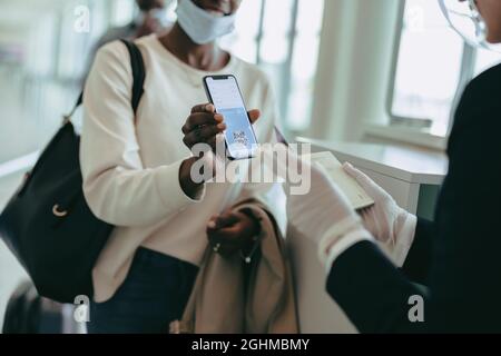 Weibliche Fluggast, die dem Flughafenpersonal einen medizinischen Pass vorweist. Bodenwächter überprüft den medizinischen Pass des Passagiers, der während einer Pandemie eincheckt. Stockfoto