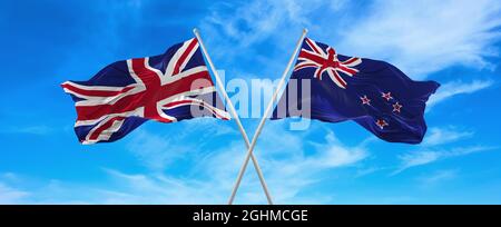 Flaggen von Großbritannien und Neuseeland winken im Wind auf Fahnenmasten gegen den Himmel mit Wolken am sonnigen Tag. Symbolisieren Beziehung, Dialog zwischen Stockfoto
