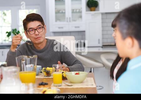 Asiatischer Vater mit Sohn und Tochter, die am Tisch sitzen und beim Frühstück ein Gespräch führen Stockfoto