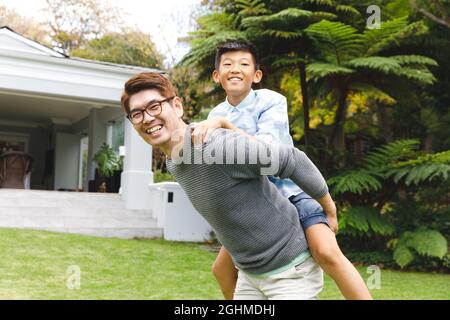 Porträt eines glücklichen asiatischen Vaters, der seinen Sohn trägt und im Garten lächelt Stockfoto