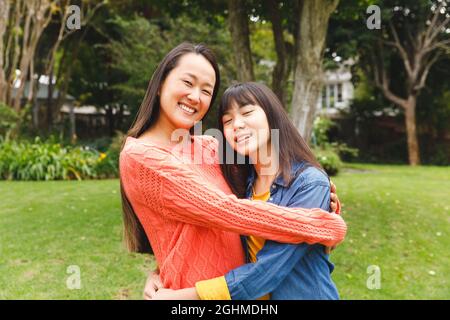 Porträt einer glücklichen asiatischen Mutter, die ihre Tochter umarmt und im Garten lächelt Stockfoto