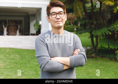 Porträt eines glücklichen asiatischen Mannes, der im Garten vor dem Haus der Familie eine Brille trägt und lächelt Stockfoto