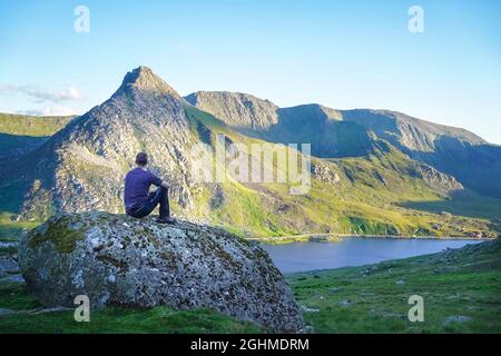 Rückansicht eines isolierten Wanderers auf Felsen mit Blick über den Lake Ogwen zum Mount Tryfan am sonnigen Sommertag, Snowdonia National Park, N. Wales, Großbritannien. Stockfoto