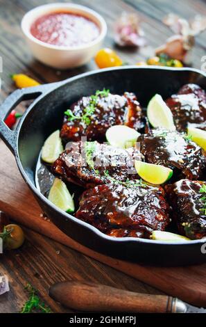 Würziges Chili Chicken Oberschenkelfleisch in einer gusseisernen Pfanne über einem Holzschneidebrett und rustikalem Hintergrund mit frischen Zutaten. Selektiver Fokus auf Huhn Stockfoto