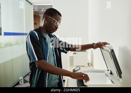 Seriöser junger schwarzer Mann, der Fotokopierer für die Erstellung von Vertragskopien für die Besprechung verwendet Stockfoto