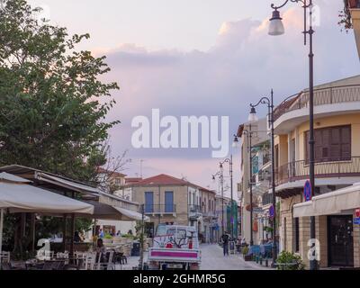 LKW-Wagen mit Fracht bewegt sich entlang der zentralen Straße der Altstadt von Larnaca mit Menschen sitzen im Café, zu Fuß in der Nähe von alten Gebäuden. Touristisches Konzept. Stockfoto