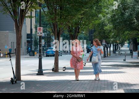 Charlotte, North Carolina, USA - 24. August 2021: Zwei Frauen in bunten Kleidern gehen und sprechen auf der Tryon Street in der Uptown Charlotte Stockfoto