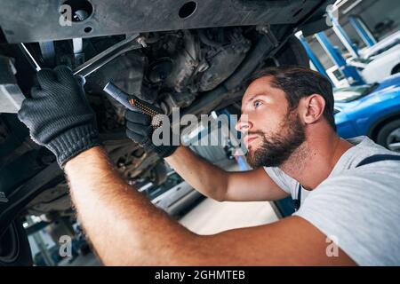 Mechaniker inspiziert die Unterseite des Autos mit Taschenlampe Stockfoto