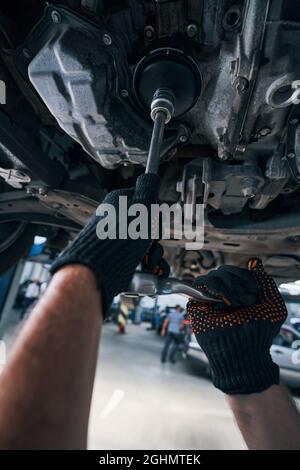 Person unter dem Fahrzeug, die den Steckschlüssel zur Durchführung der Überprüfung verwendet Stockfoto