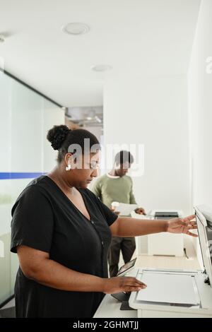 Seriöser Büroleiter, der Kopien von Berichten und wichtigen Dokumenten für Mitarbeiter erstellt Stockfoto