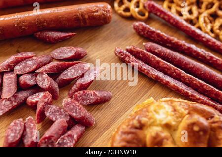 Nahaufnahme von Bier-Snacks, geräucherten Würstchen und Brezeln auf Holztablett. Draufsicht. Oktoberfest-Feiertagsküche. Traditionen, Spaß, Freude, Essen und Trinken. Stockfoto