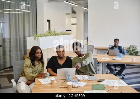 Gruppe von jungen schwarzen Geschäftsleuten, die bei der Besprechung die Produktpräsentation auf dem Bildschirm des Laptops ansehen Stockfoto