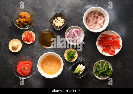 Viele thailändische Zutaten für das Gericht Gai Pad Pongali mit Huhn, Eier, würzige, gelbe thai-Nudeln, Tomaten, Reis in schwarzer Schüssel im Wok gemacht. Traditionell Stockfoto