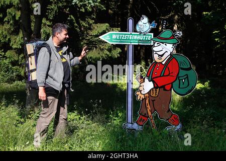 Wanderer und Schild Wetzsteinhütte, Mann mit Rucksack vor Wegweiser am Altvaterturm am Wetzstein, Mahnmal gegen die Vertreibung von Menschen Stockfoto