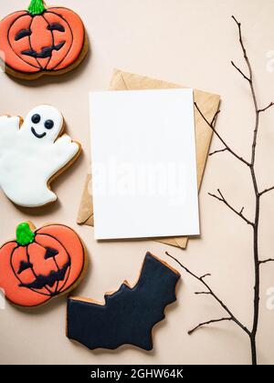 Leere weiße Postkarte und Bastelumschlag und Halloween Lebkuchen - Jack O'Lantern, Fledermaus und Geist auf beigem Hintergrund. Halloween-Konzept. Oben Stockfoto