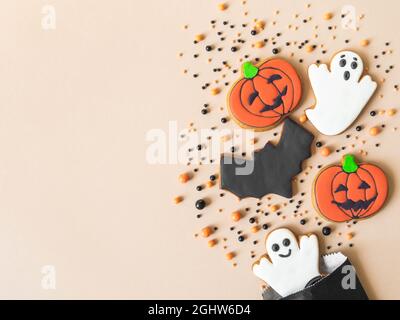 Verschiedene Halloween Lebkuchenkekse - Jack O'Lantern, Geister, Fledermaus und Zucker streut von Papiertüte auf beigem Hintergrund. Minimales Halloween Stockfoto